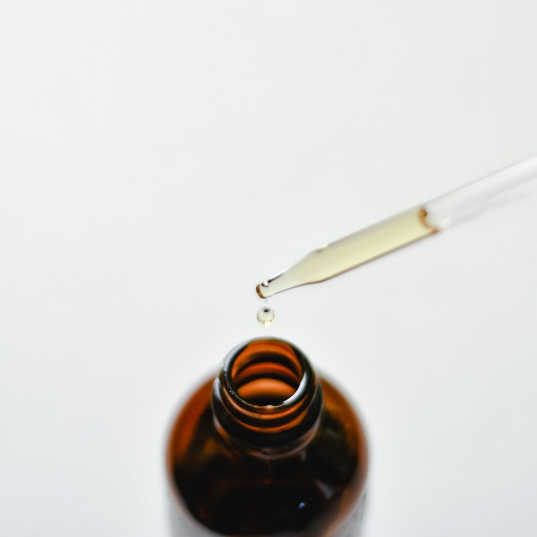 Brown glass bottle with dropper full of essential oil on a white background