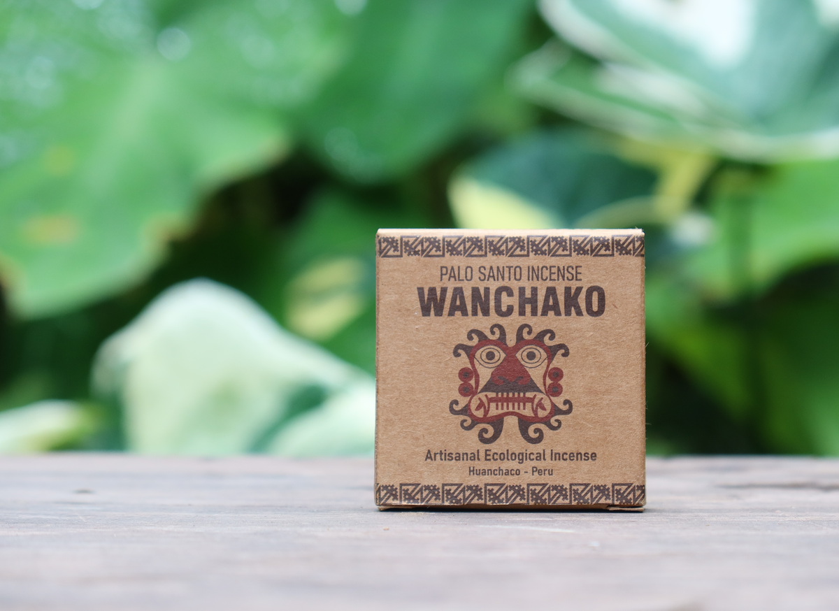 Wanchako Palo Santo Incense box on a wooden surface with blurred green foliage in the background
